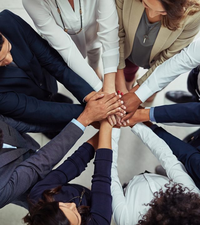 High angle shot of a group of businesspeople joining their hands together in unity.
