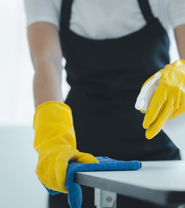 Cleaning desk surface in office with sanitizer spray, wear gloves and wipe the table with a towel, the housekeeper is cleaning the work desk for hygiene because of the Covid-19, cleaning idea.